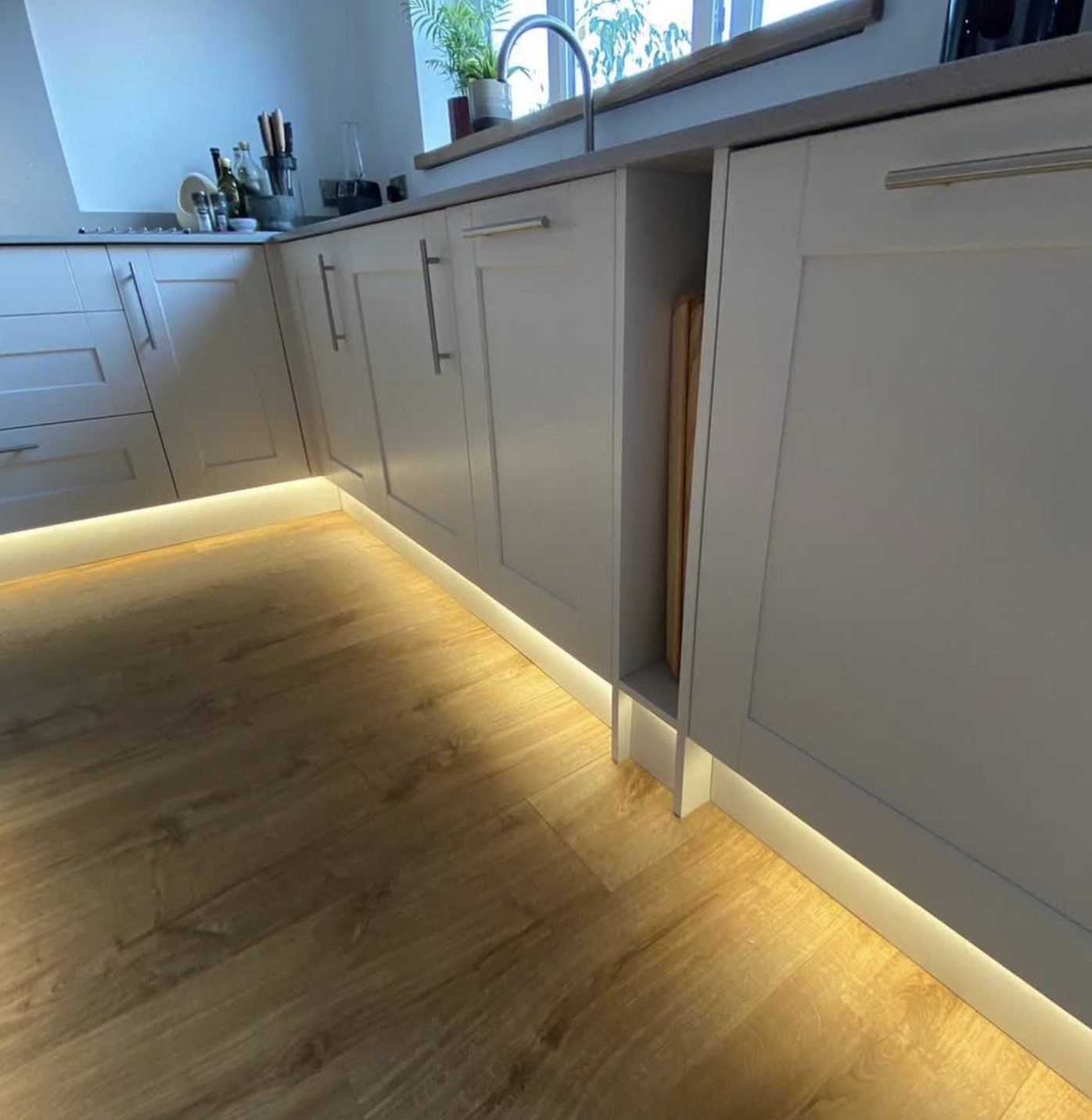 Warm LED plinth lighting washing across a kitchen floor
